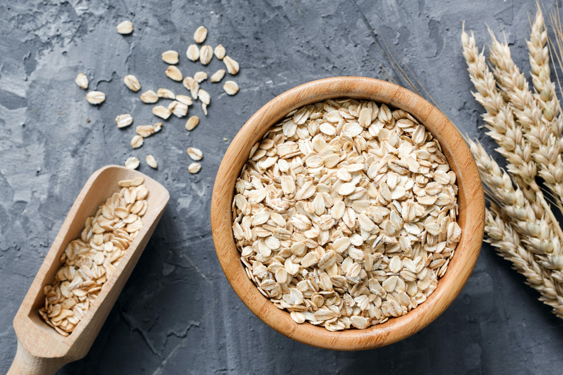 Rolled oats or oat flakes in wooden bowl and golden wheat ears