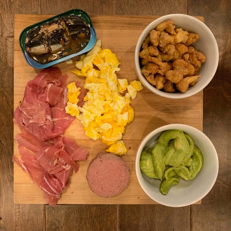 Dinner plate with canned sardines, uncured prosciutto, guacamole, liverwurst, scrambled eggs and cauliflower bites