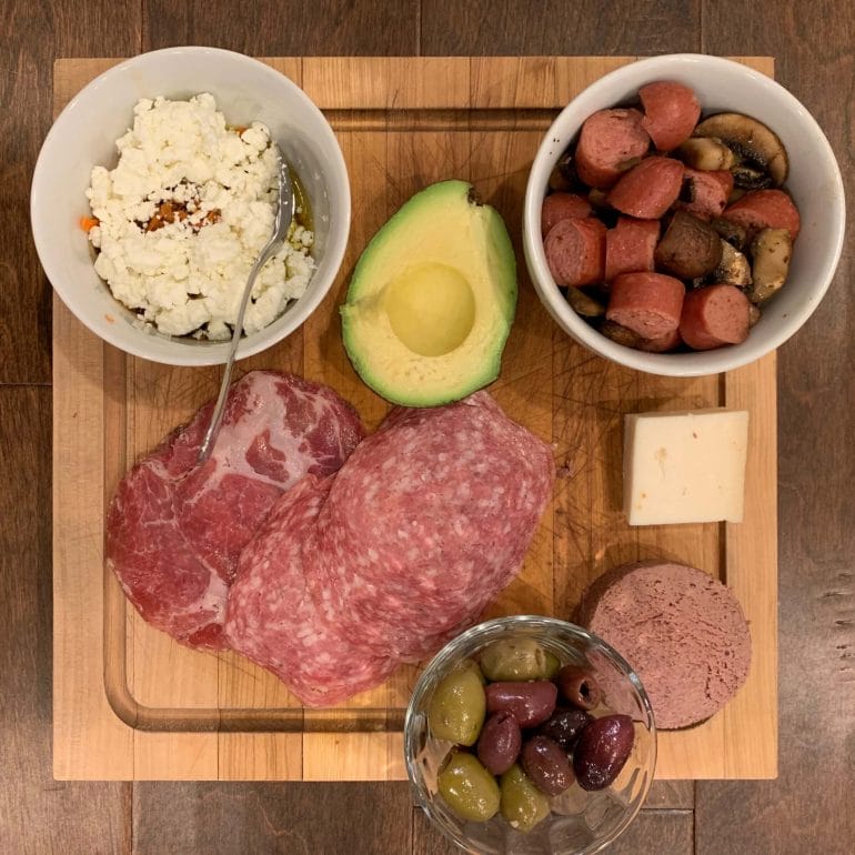 Dinner plate with uncured cold cuts, liverwurst, olives, sausages, goat cheese, mushrooms and a mix of goat cheese crumbles with carrots and a lot of olive oil