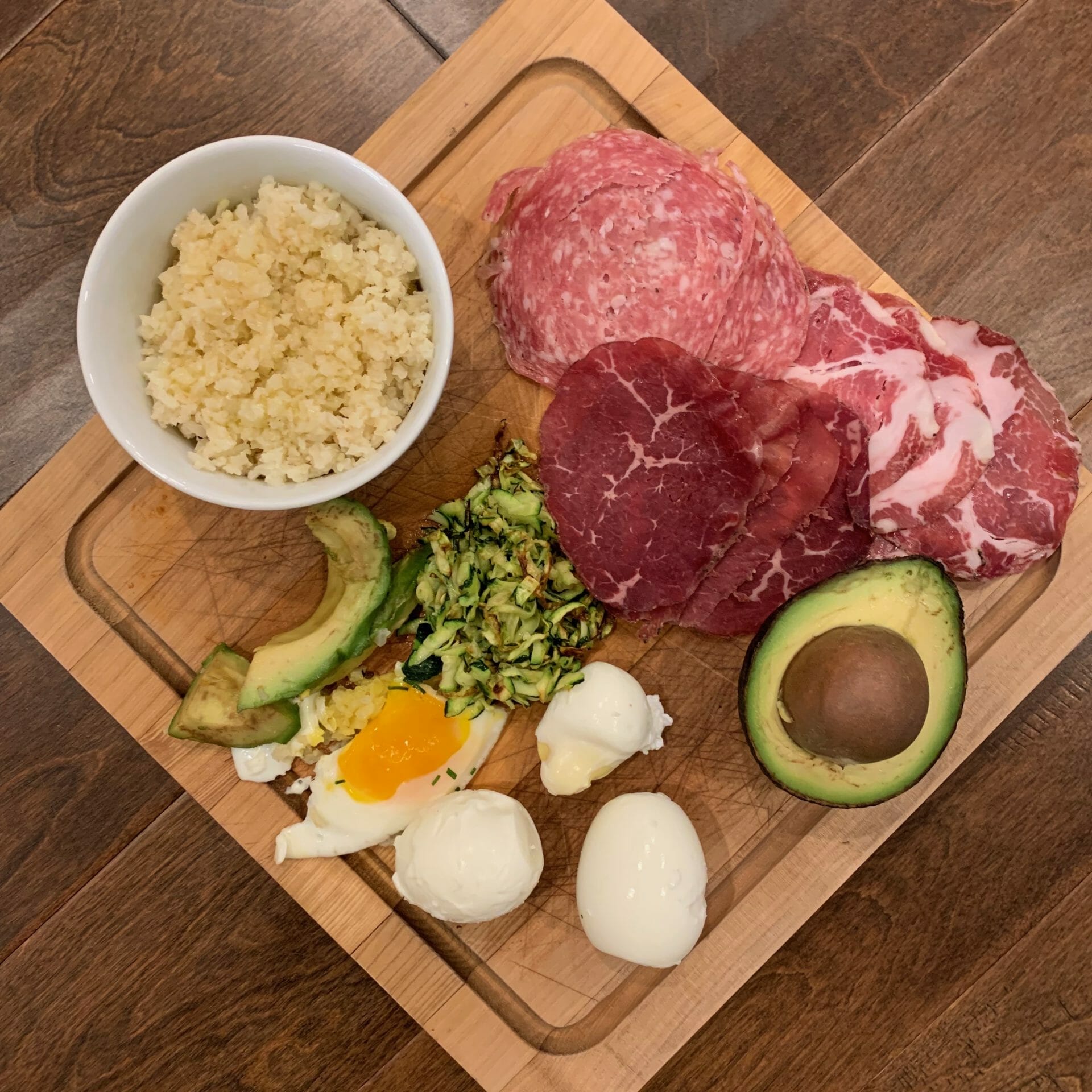 Dinner plate with riced cauliflower, uncured meats, avocado, soft-boiled eggs and riced zucchini