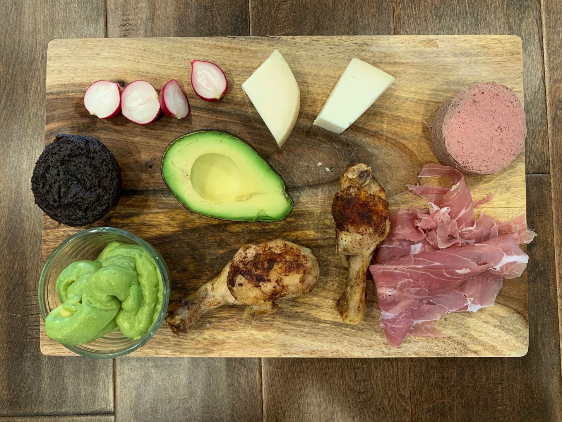 Dinner plate with uncured prosciutto, chicken thighs, avocado, liverwurst, guacamole, goat cheese, radishes and a paleo muffin