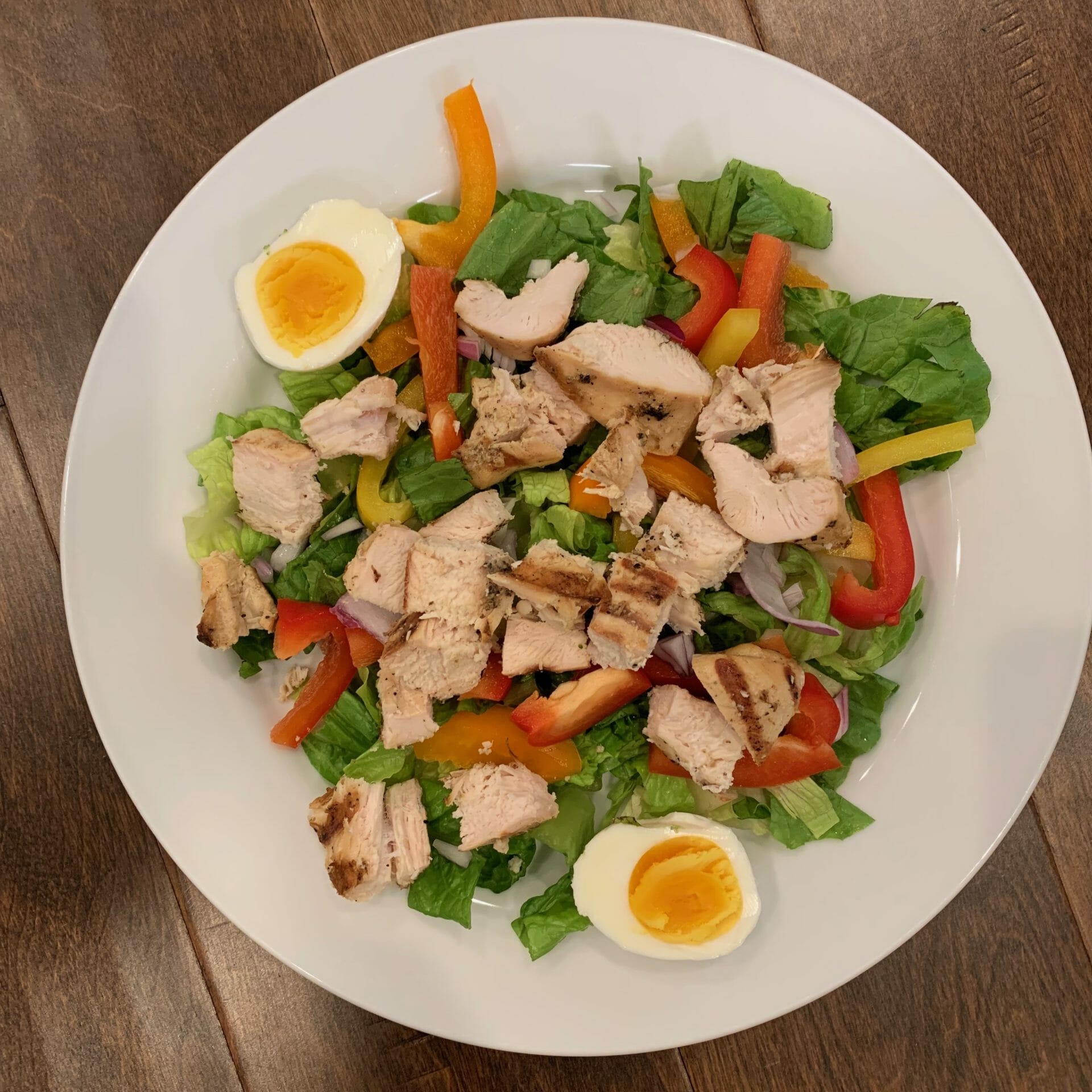Salad with chunks of grilled chicken, lettuce, boiled eggs, peppers and onions