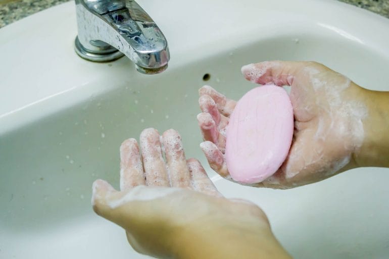 Hand holding a bar of soap under a faucet