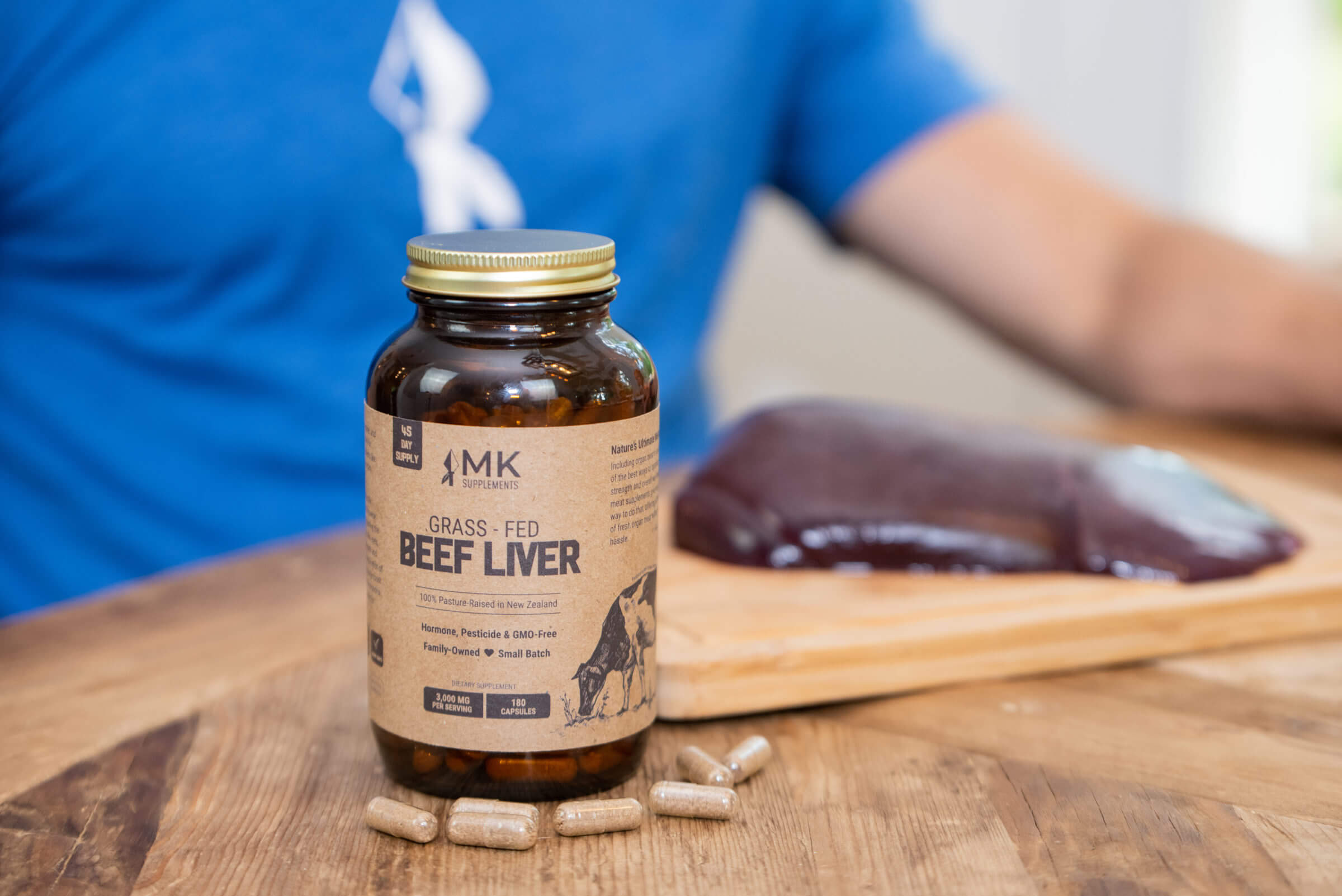 Photo of MK Supplements grass-fed beef liver supplements bottle with pills on table.