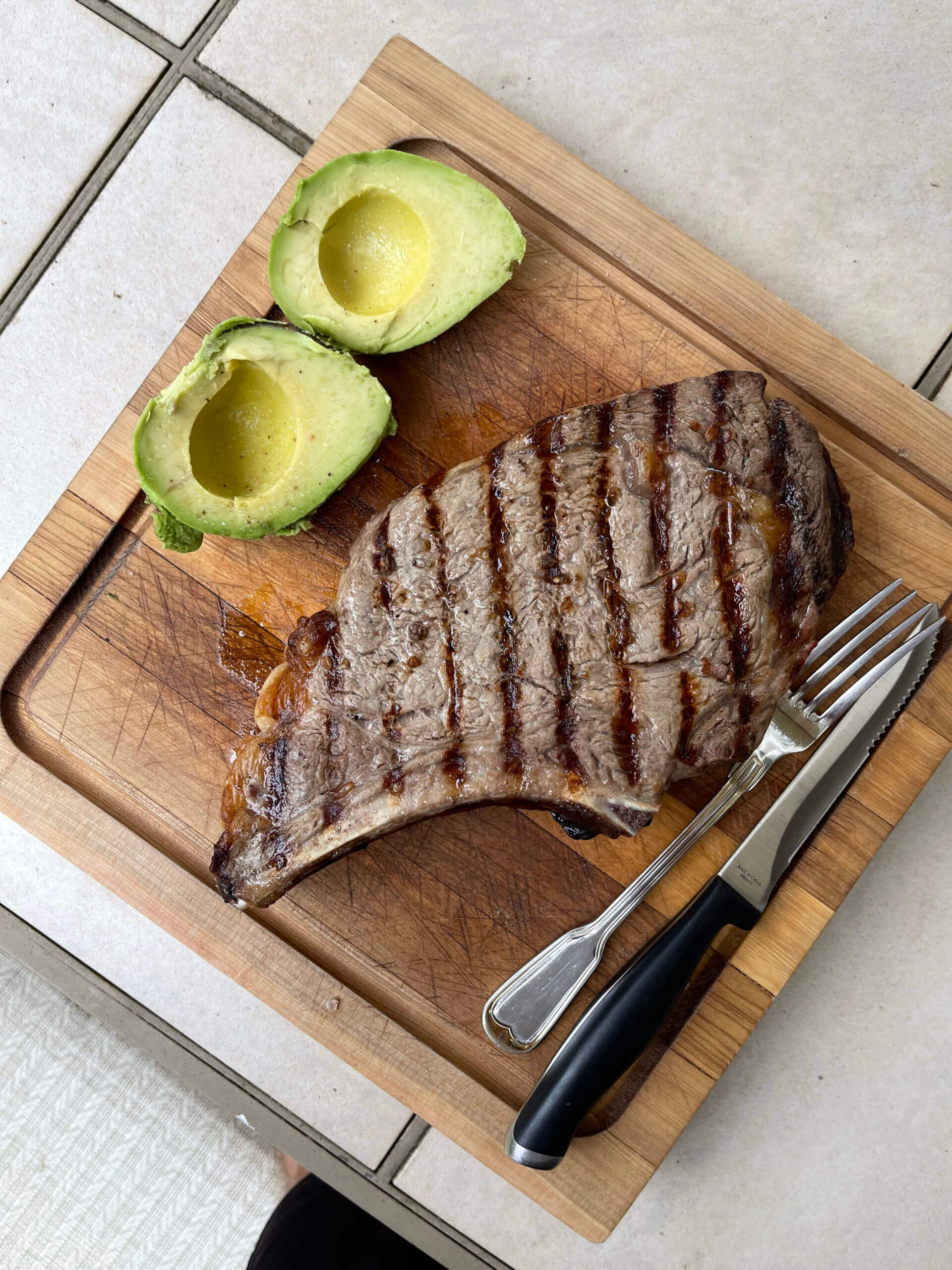 Photo of a steak and avocado with silverware on a cutting board.