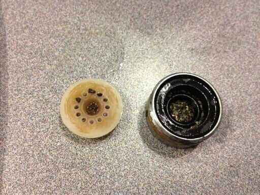 Photo of the inside of a faucet aerator with black slime buildup. 