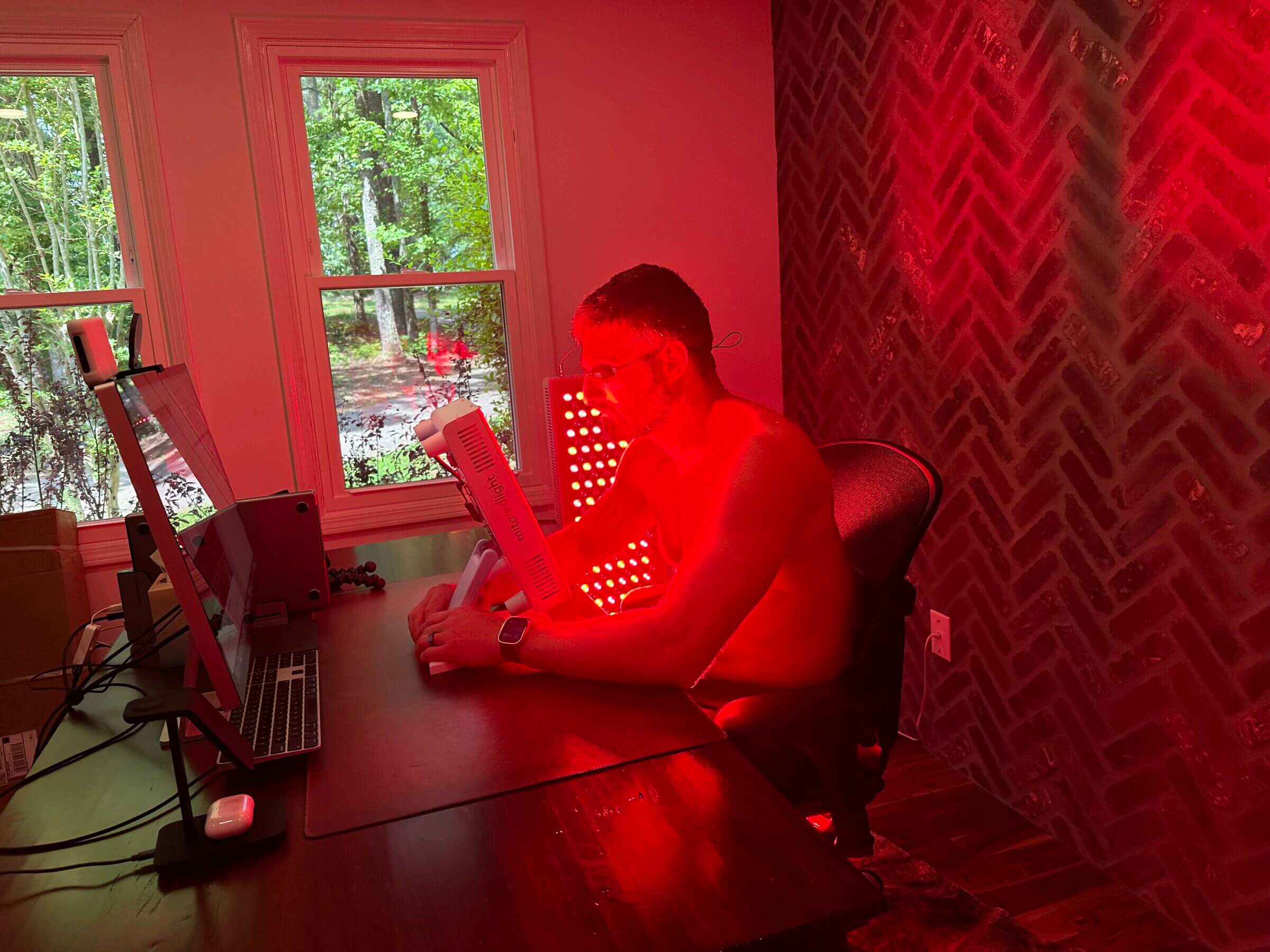 A picture of Michael sitting at his desk using a MItoPro 300 red light panel.