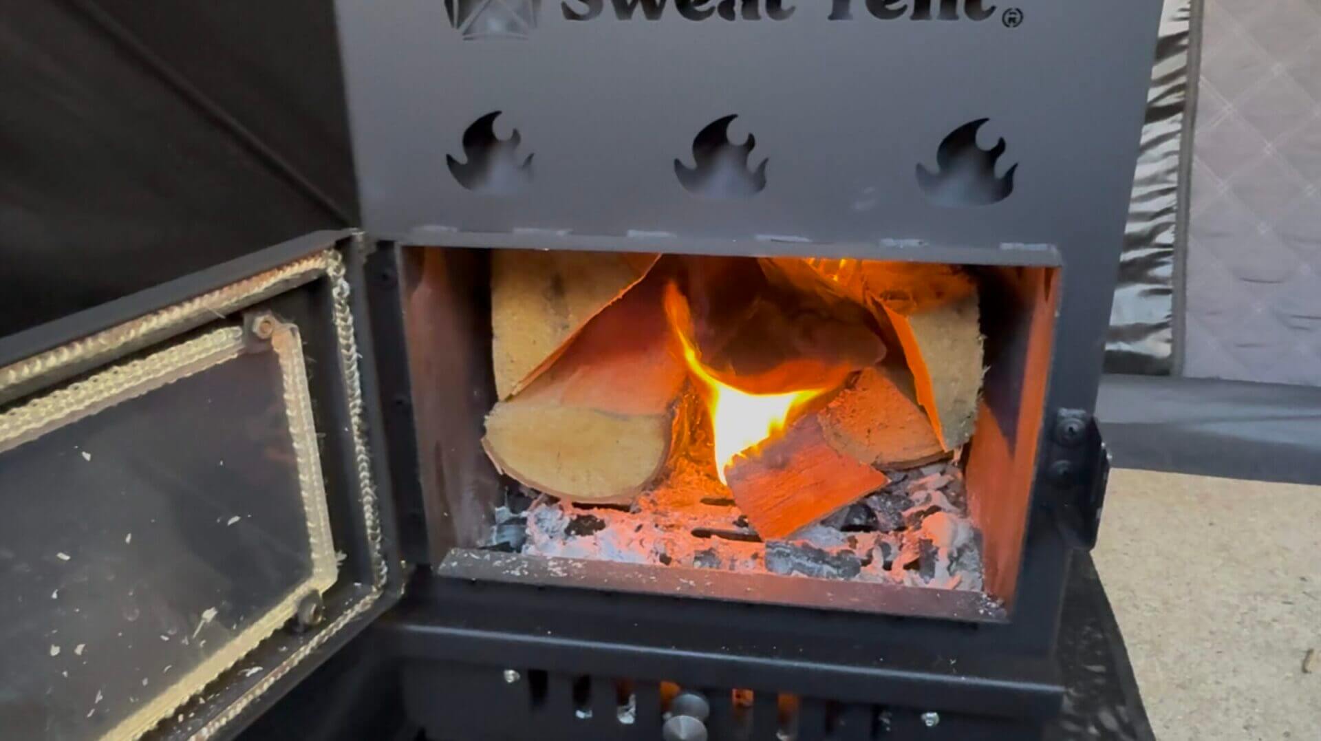 The Sweat Tent stove burning logs.