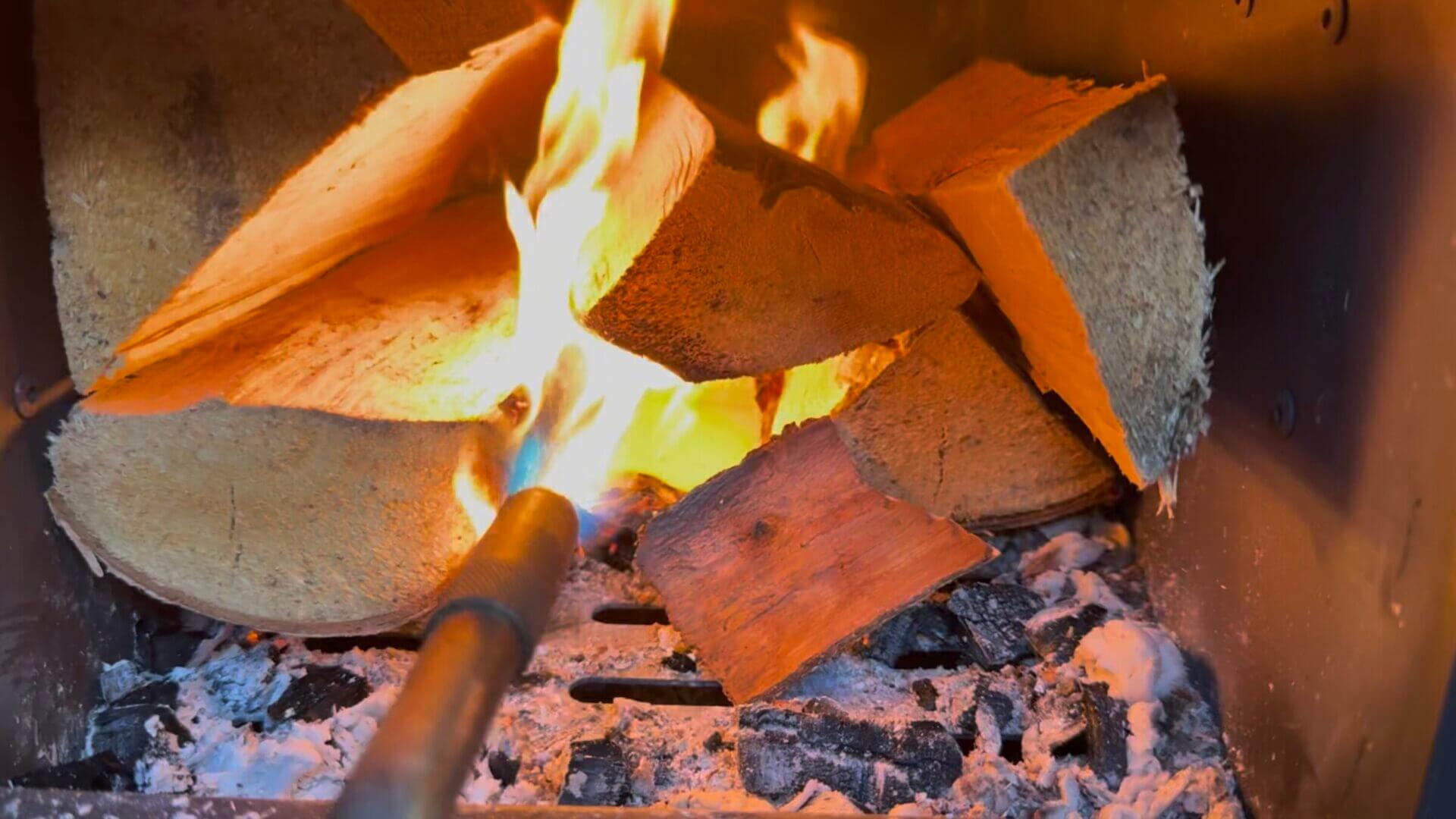 Lighting wood logs on fire with a torch, inside the Sweat Tent sauna's heater.