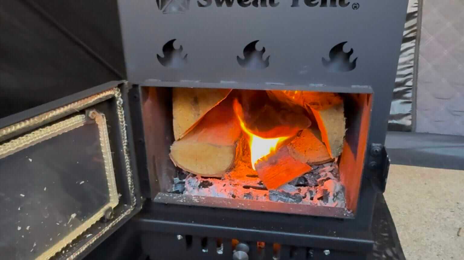 Wood logs burning inside the Sweat Tent sauna heater.